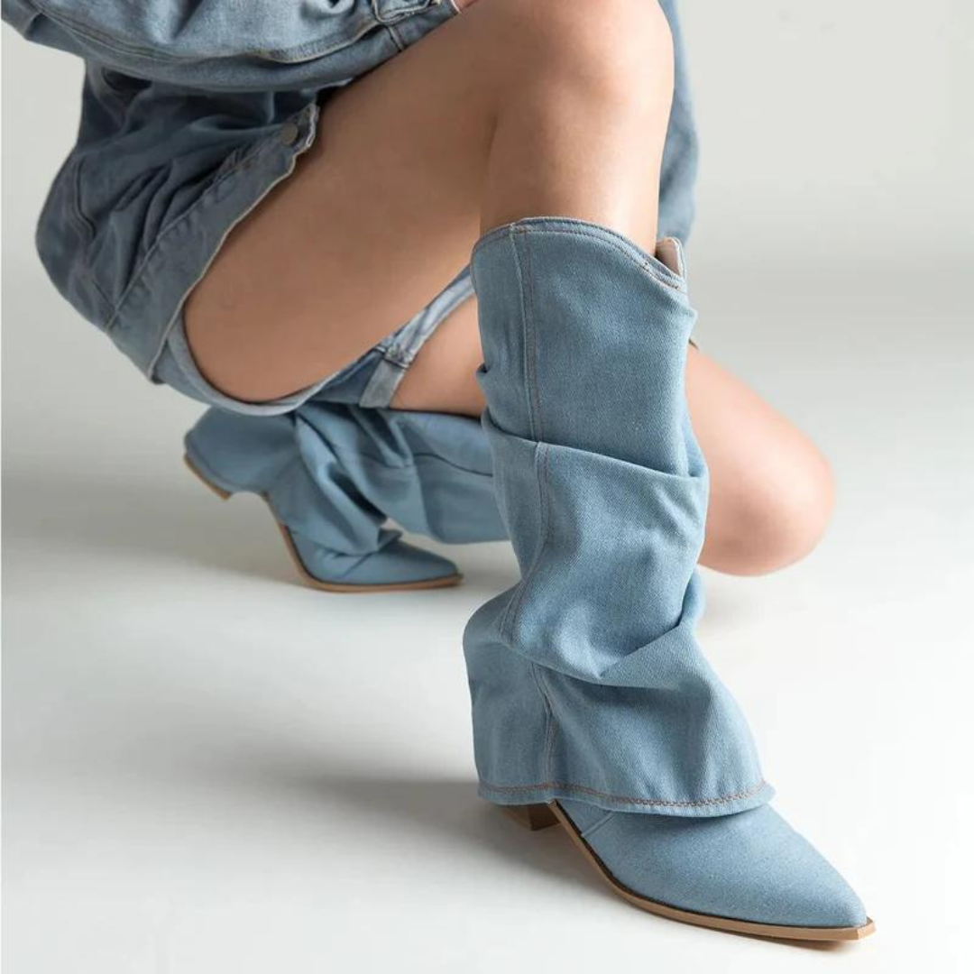 Stivali in denim azzurro con tacco basso, design moderno e pieghe morbide, indossati con abbigliamento coordinato, moda autunno-inverno.
