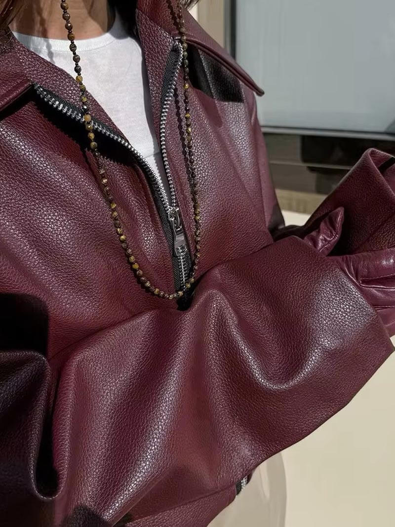 Giacca in pelle bordeaux con zip, indossata sopra una maglietta bianca, accessoriata con collana di perline. Moda autunnale elegante.