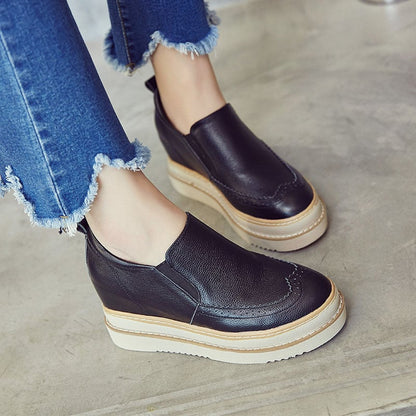 Scarpe slip-on nere in pelle con zeppa, indossate con jeans strappati. Calzature moda donna, comode e casual, ideali per look quotidiani.