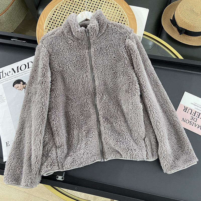 Giacca in pile grigio su tavolo nero, accanto a rivista e cappello di paglia. Moda autunnale, abbigliamento caldo, stile casual.