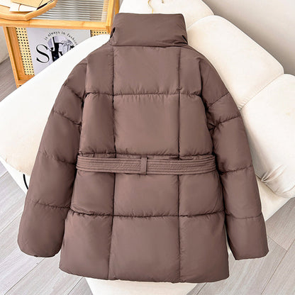 Giacca invernale imbottita marrone su divano beige, design trapuntato, cintura in vita, ideale per moda autunno-inverno, abbigliamento caldo donna.
