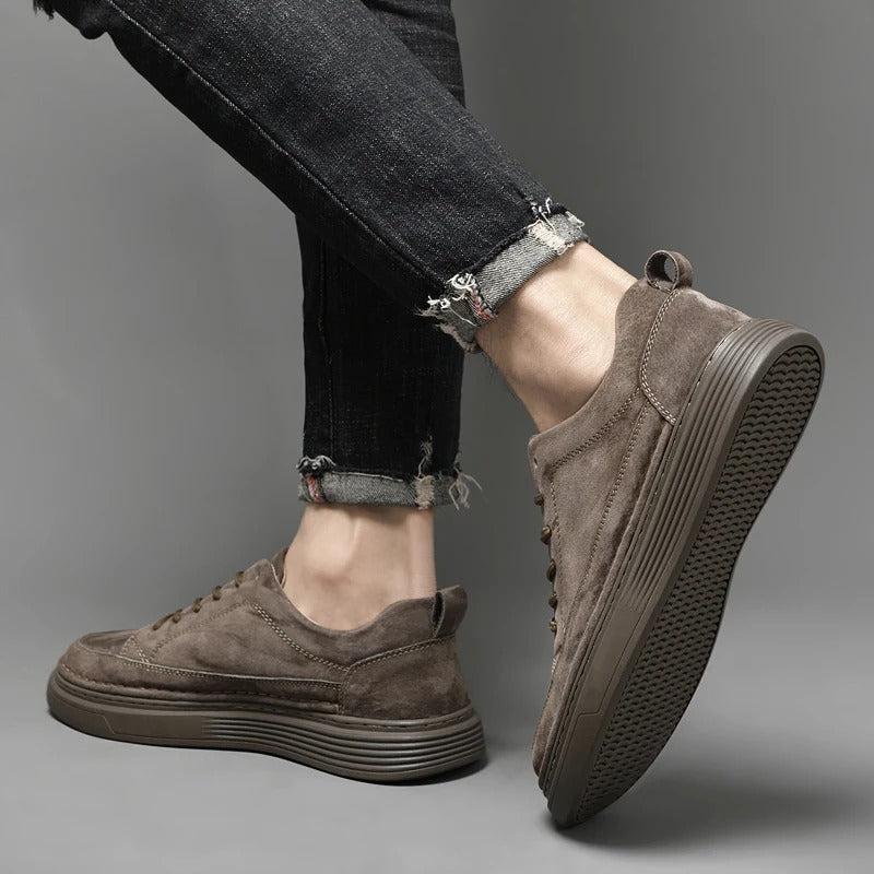 Scarpe da ginnastica in pelle scamosciata marrone, suola antiscivolo, indossate con jeans neri strappati. Stile casual, moda uomo, calzature trendy.