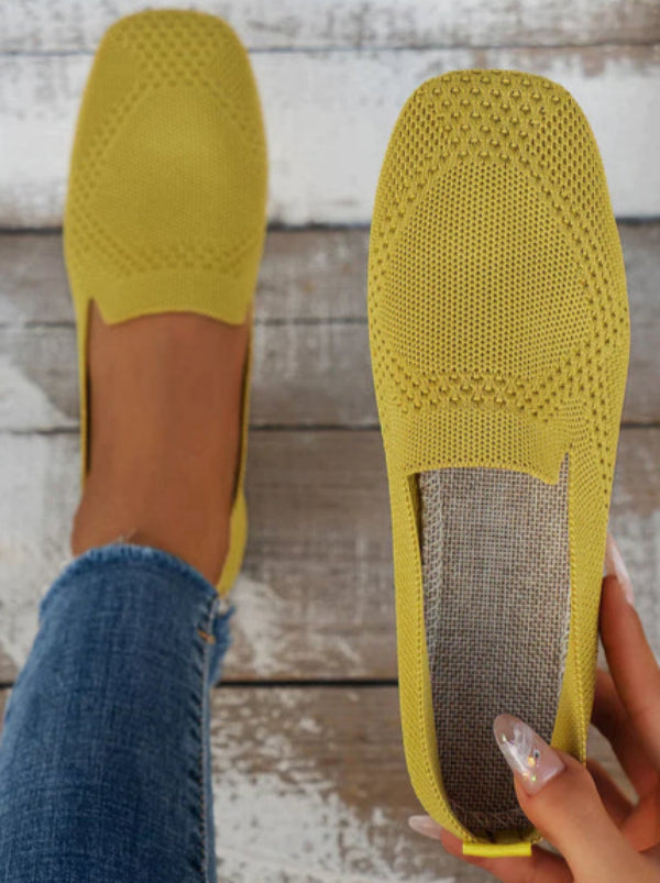 Scarpe gialle in maglia traspirante su pavimento in legno, indossate con jeans. Design casual, comode e alla moda per look estivo.