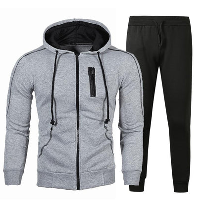 Tuta sportiva uomo, felpa grigia con cappuccio e zip, pantaloni neri. Abbigliamento casual, comodo per palestra e tempo libero.