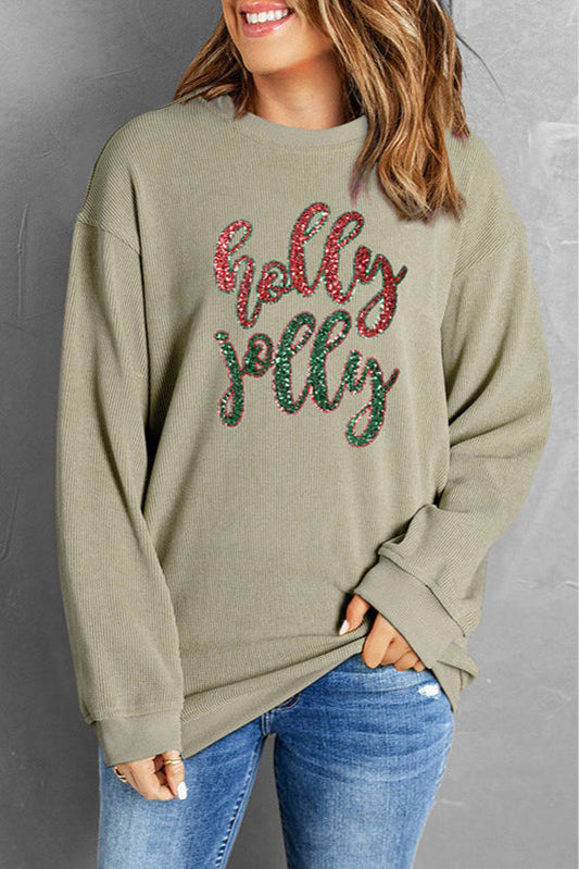 Donna sorridente con maglione grigio con scritta "holly jolly", jeans blu, sfondo grigio. Moda casual autunnale, abbigliamento comodo.