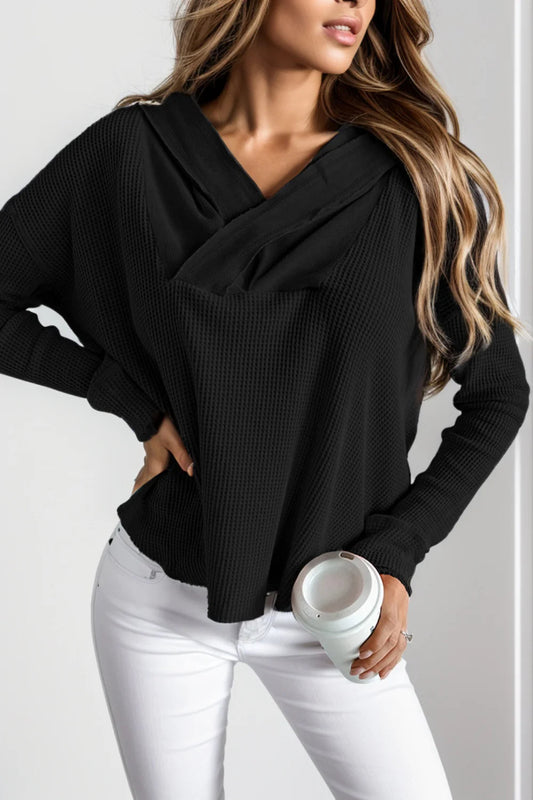 Donna con maglione nero a trama larga, pantaloni bianchi, tiene una tazza da caffè. Moda casual autunnale, look elegante e moderno.