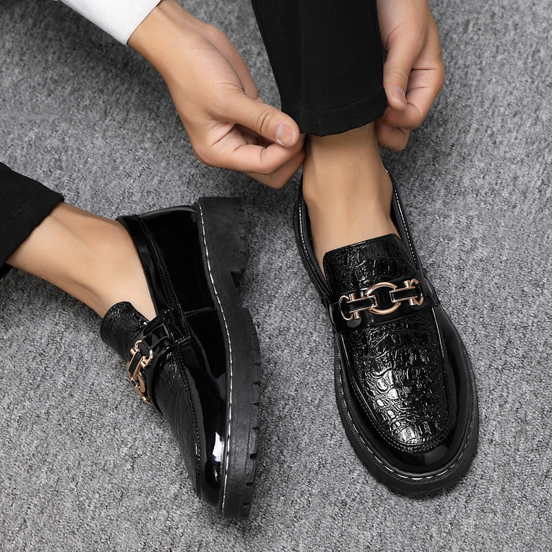 Scarpe eleganti uomo in pelle nera lucida con dettaglio catena metallica, indossate su pavimento grigio. Scarpe formali moda maschile.