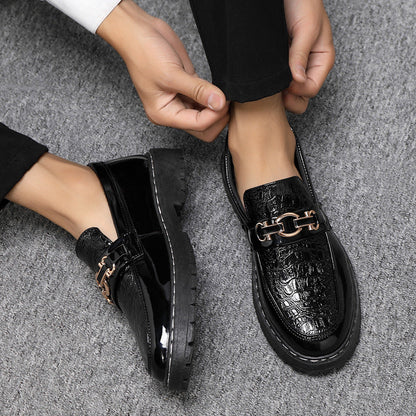 Scarpe eleganti uomo in pelle nera lucida con dettaglio catena metallica, indossate su pavimento grigio. Scarpe formali moda maschile.
