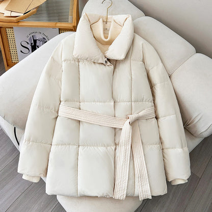 Giacca invernale bianca imbottita con cintura, appesa su appendiabiti. Design trapuntato, ideale per moda donna e abbigliamento caldo.