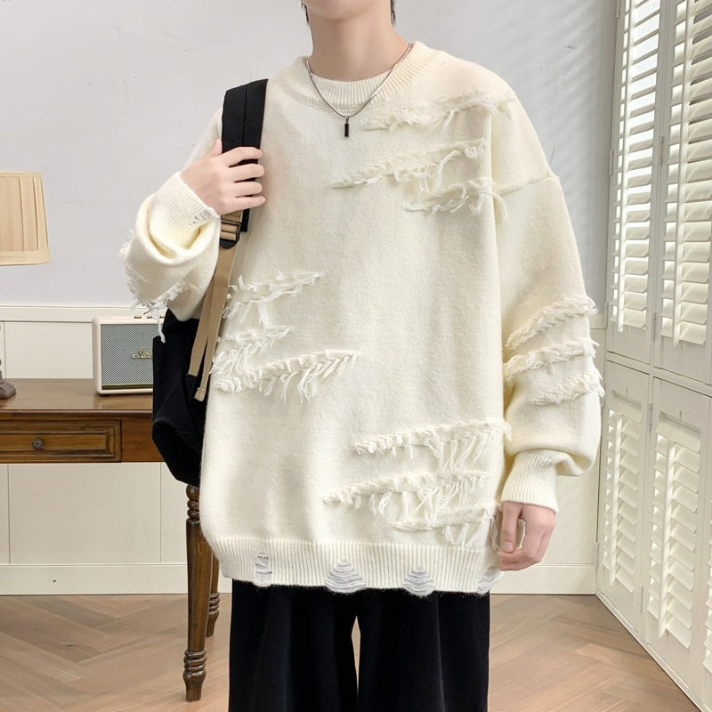 Maglione bianco oversize con dettagli sfrangiati, indossato da una persona con zaino nero. Sfondo con scrivania in legno e lampada. Moda casual.