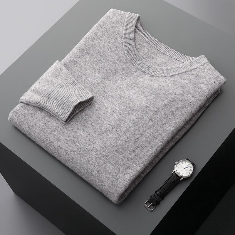 Maglione grigio piegato su tavolo nero, accanto a orologio da polso con cinturino in pelle nera. Elegante abbigliamento invernale maschile.