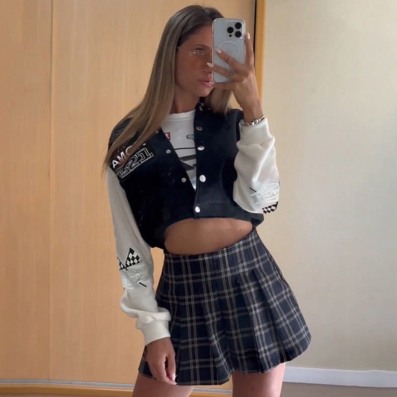 Giovane donna in posa davanti a uno specchio, indossa una giacca sportiva nera e bianca e una gonna a quadri. Scatta un selfie con uno smartphone.