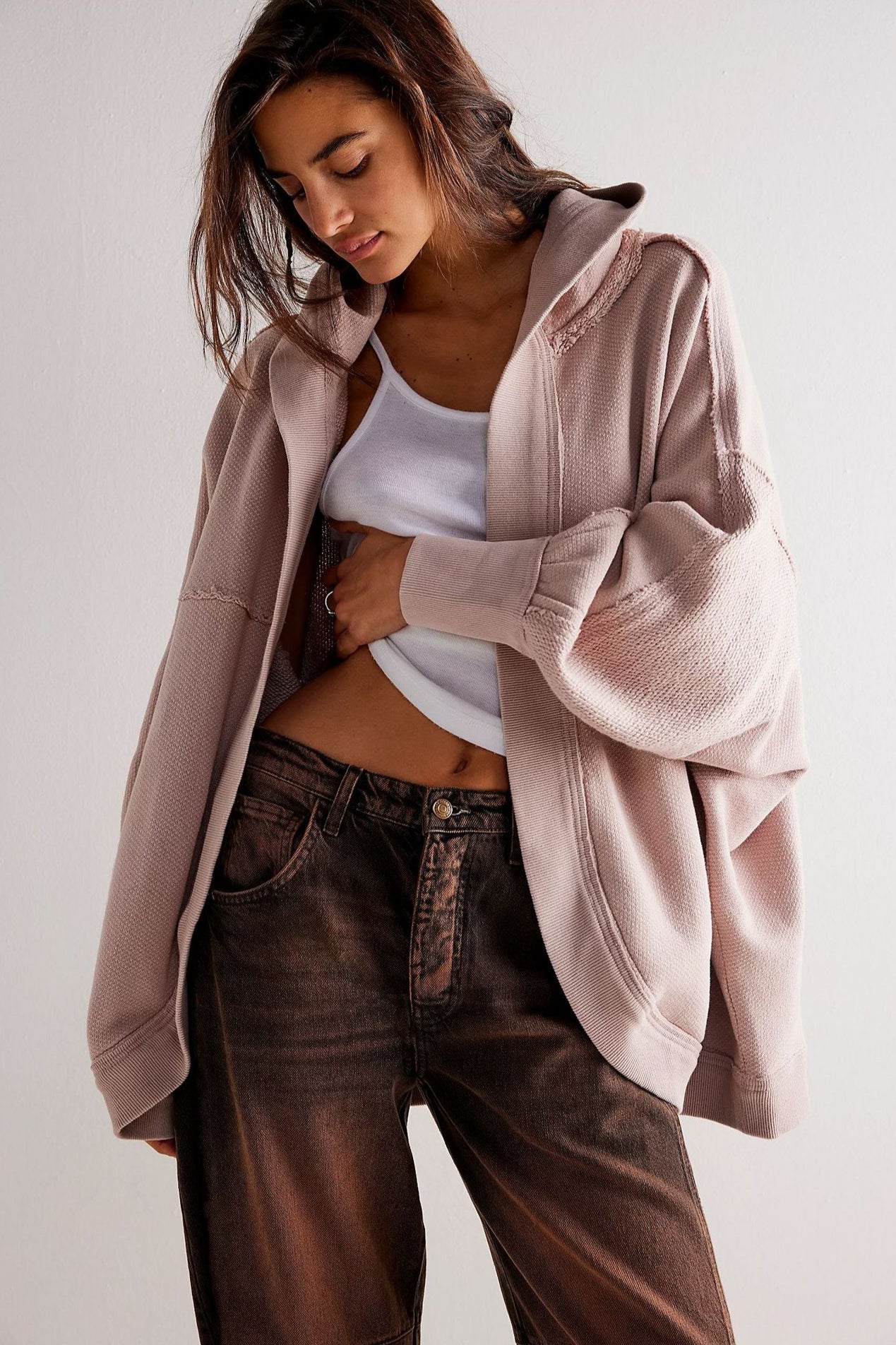 Donna con felpa oversize rosa e jeans marroni, posa casual. Moda autunnale, abbigliamento comodo, stile urbano.