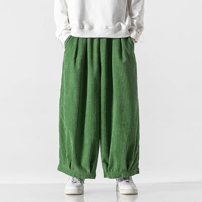 Pantaloni verdi a coste larghe, indossati con felpa bianca e scarpe da ginnastica bianche. Moda casual, stile urbano, abbigliamento comodo.