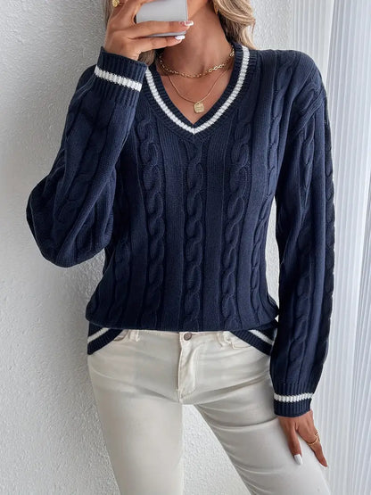 Maglione blu a trecce con scollo a V e dettagli bianchi, indossato con jeans bianchi. Stile casual elegante, moda autunnale donna.