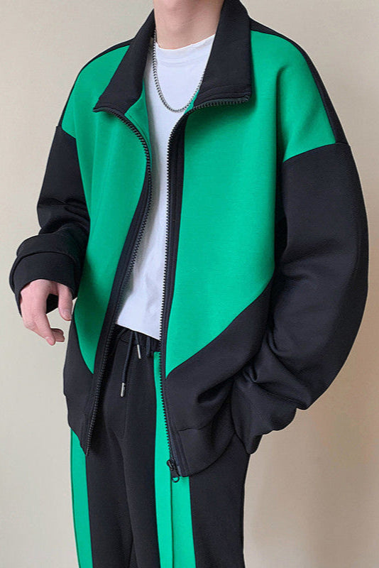 Giacca sportiva verde e nera da uomo, stile casual, con zip aperta e maglietta bianca sotto. Abbigliamento moda streetwear, tuta coordinata.