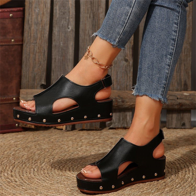 Sandali neri con zeppa e borchie, indossati con jeans strappati. Scarpe estive alla moda, perfette per un look casual e trendy.
