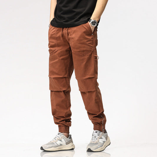 Pantaloni cargo marroni da uomo, stile casual, con tasche multiple, indossati con scarpe da ginnastica grigie e maglietta nera.