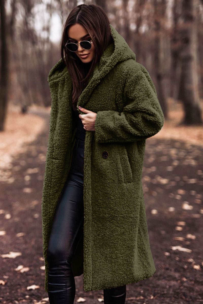 Donna con cappotto verde in pelliccia sintetica, occhiali da sole, pantaloni neri in pelle, passeggia in un parco autunnale. Moda autunno inverno.
