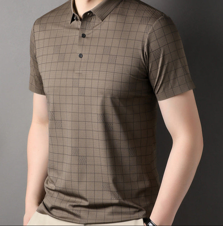 Maglietta polo marrone a quadri, maniche corte, colletto classico, bottoni neri, indossata da uomo su sfondo grigio. Moda casual elegante.