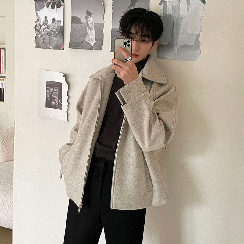 Giovane uomo con giacca beige e smartphone, posa davanti a muro con foto in bianco e nero. Moda autunnale, stile casual elegante.