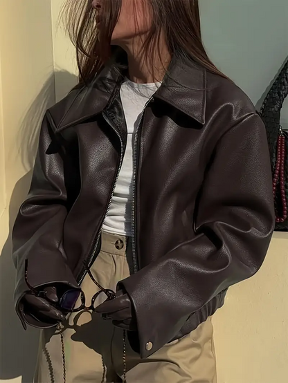 Donna con giacca di pelle marrone, maglietta bianca e pantaloni beige, tiene occhiali da sole. Moda autunnale, stile casual chic.