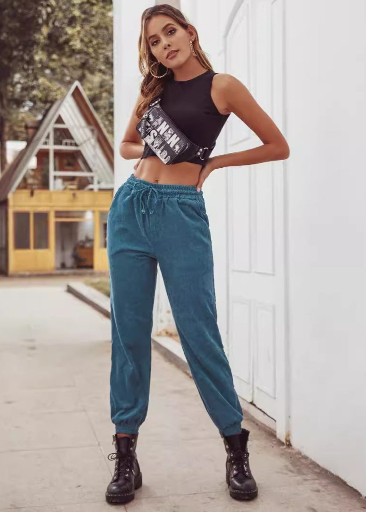 Donna con top nero e pantaloni blu, borsa a tracolla, stivali neri, posa all'aperto. Moda casual, abbigliamento urbano, stile giovanile.