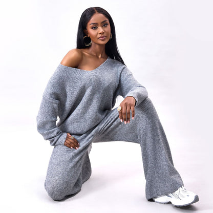Donna in posa con abbigliamento casual grigio, maglione oversize e pantaloni larghi, su sfondo bianco. Stile moda autunnale, comfort ed eleganza.