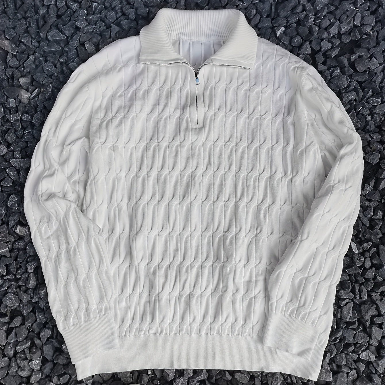 Maglione bianco a collo alto con zip, motivo a trecce, su sfondo di pietre scure. Elegante e caldo, ideale per moda autunno-inverno.