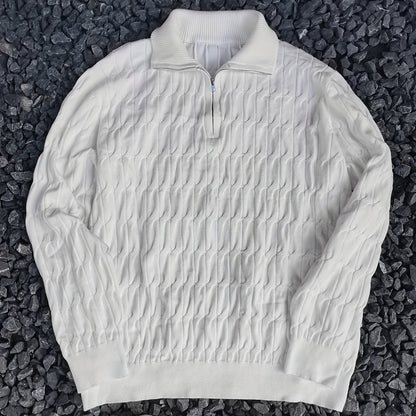 Maglione bianco a collo alto con zip, motivo a trecce, su sfondo di pietre scure. Elegante e caldo, ideale per moda autunno-inverno.