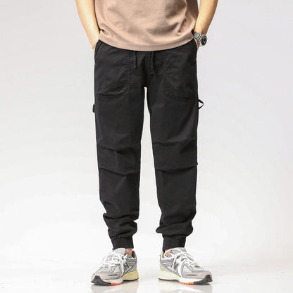 Pantaloni cargo neri da uomo con tasche multiple, indossati con sneakers bianche e grigie. Stile casual, moda maschile, abbigliamento urbano.