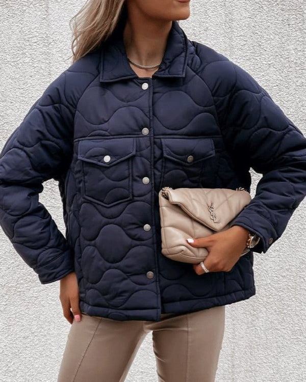 Donna con giacca trapuntata blu scuro, pantaloni beige e borsa a mano beige. Moda autunnale, stile casual chic, tendenze abbigliamento femminile.