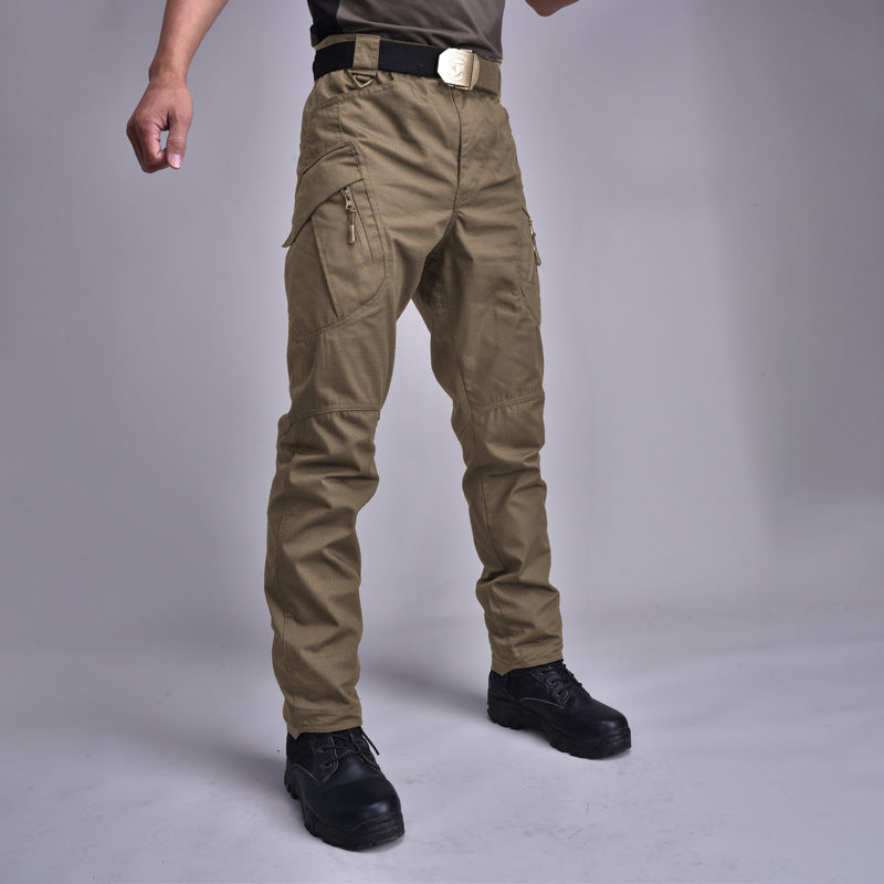 Pantaloni cargo tattici marroni, tasche multiple, indossati con cintura nera e stivali neri. Abbigliamento outdoor resistente e funzionale.