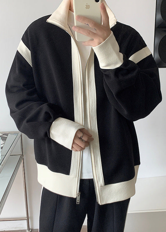 Giacca sportiva nera con dettagli bianchi, zip frontale, indossata da persona che scatta selfie con smartphone. Moda casual, abbigliamento autunnale.