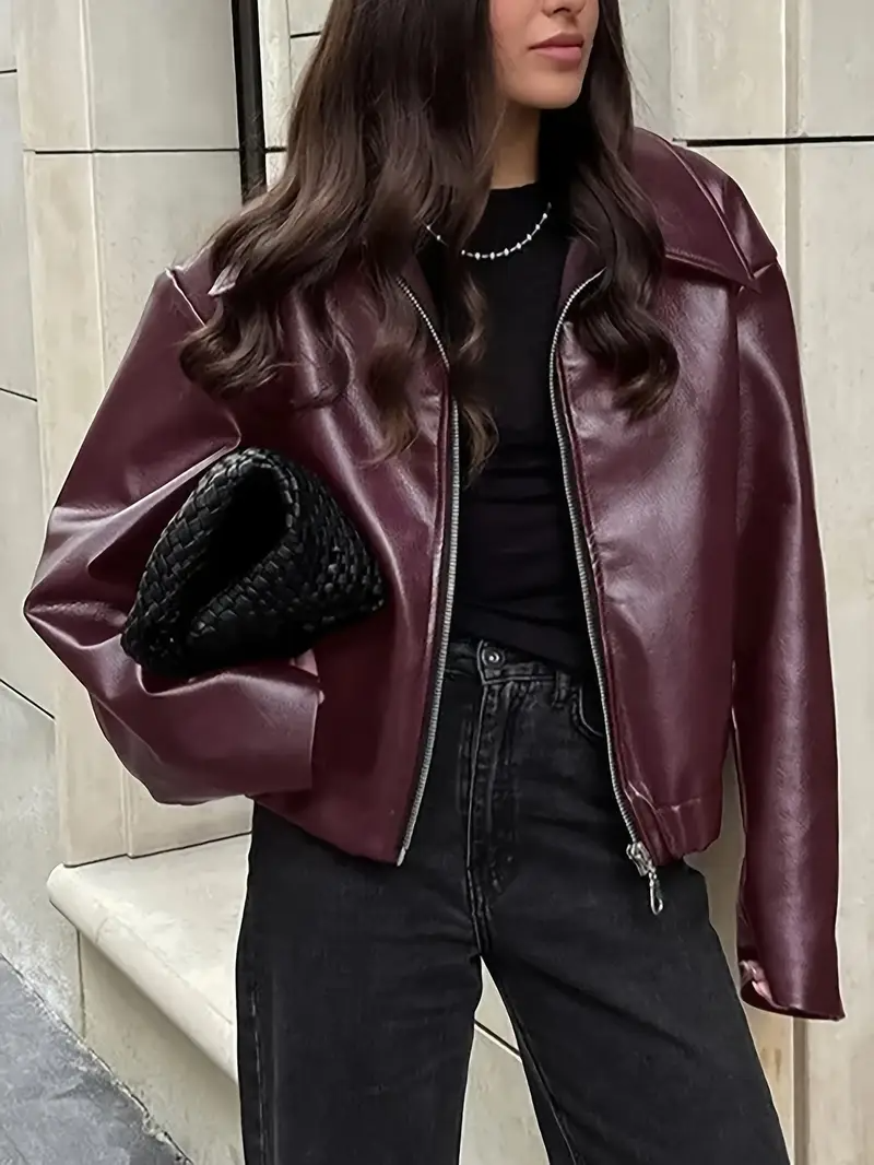 Giacca in pelle bordeaux, donna con capelli lunghi, borsa intrecciata nera, jeans neri. Moda autunnale, stile urbano elegante.
