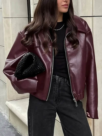 Giacca in pelle bordeaux, donna con capelli lunghi, borsa intrecciata nera, jeans neri. Moda autunnale, stile urbano elegante.