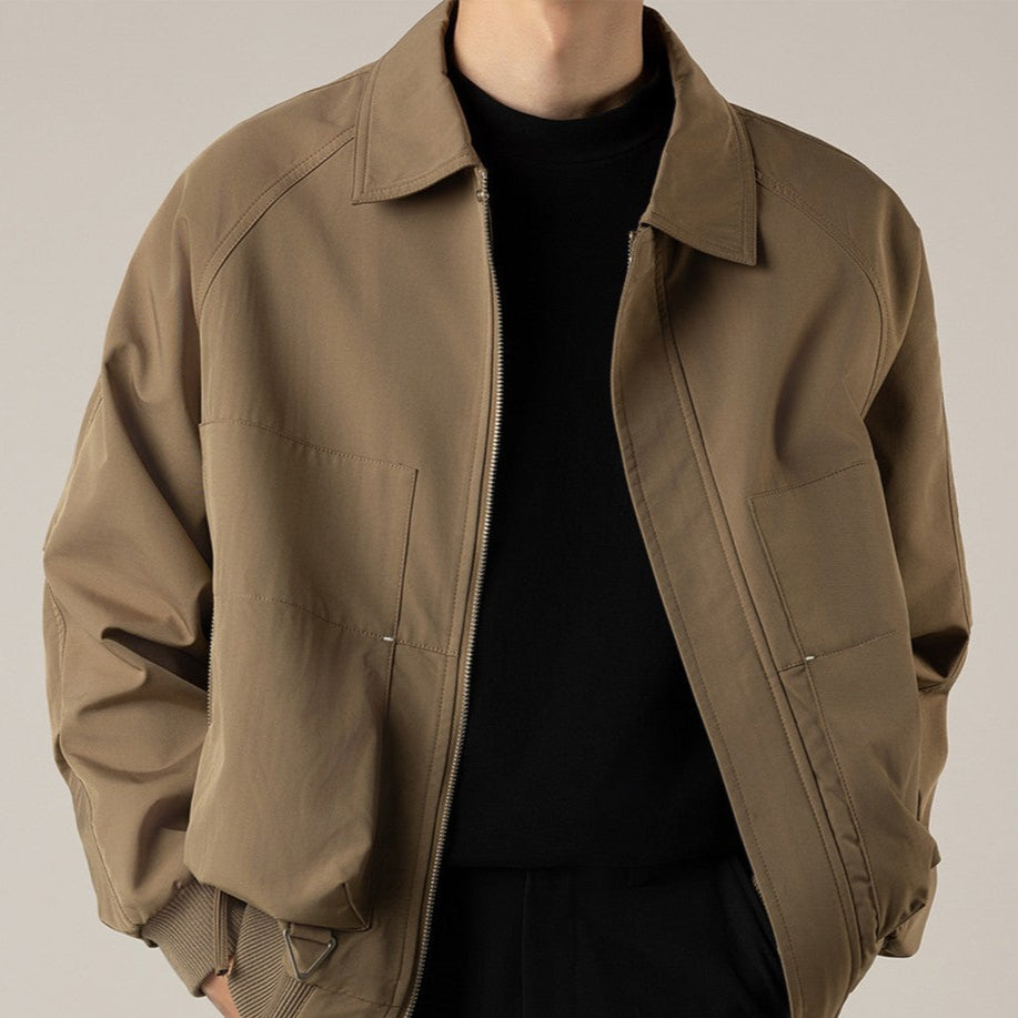 Giacca marrone chiaro da uomo, stile casual, con cerniera e tasche frontali, indossata su maglia nera. Moda maschile autunnale elegante.