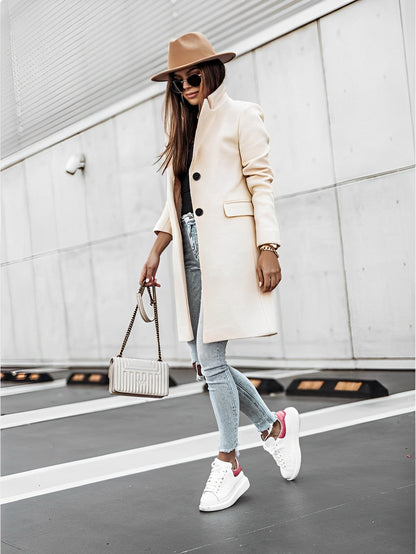Donna alla moda con cappotto beige, jeans strappati, sneakers bianche e cappello marrone, cammina su strada urbana. Stile autunnale elegante.