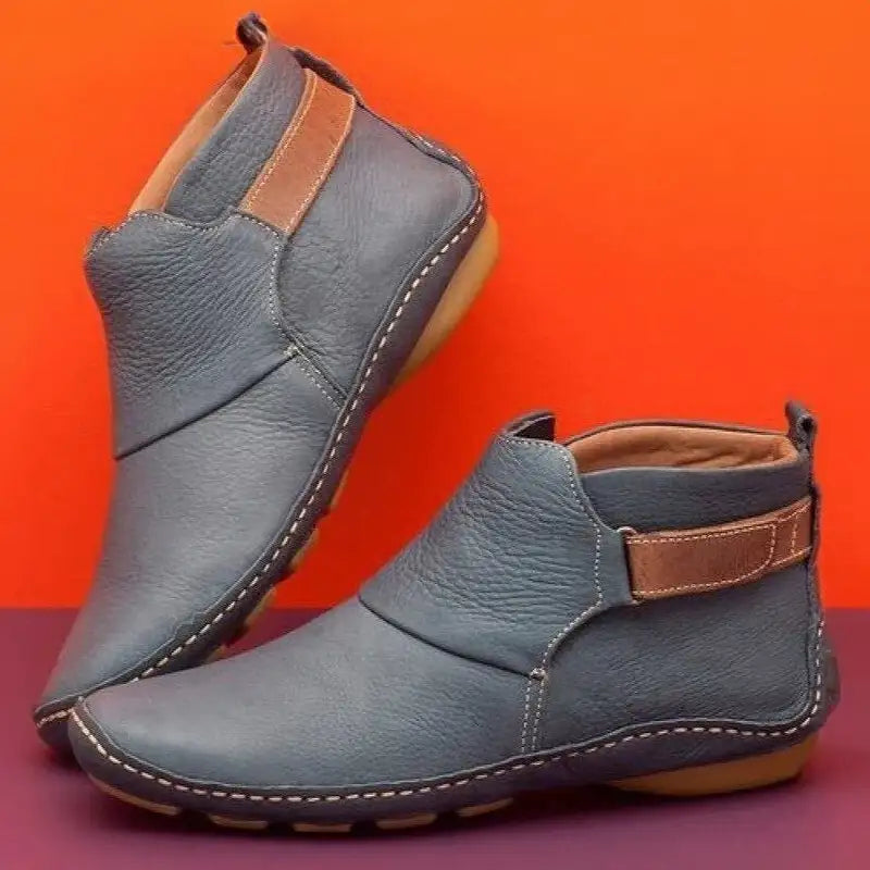 Stivaletti in pelle blu con suola in gomma beige, design moderno e cuciture a vista, sfondo arancione e viola. Scarpe eleganti e casual.