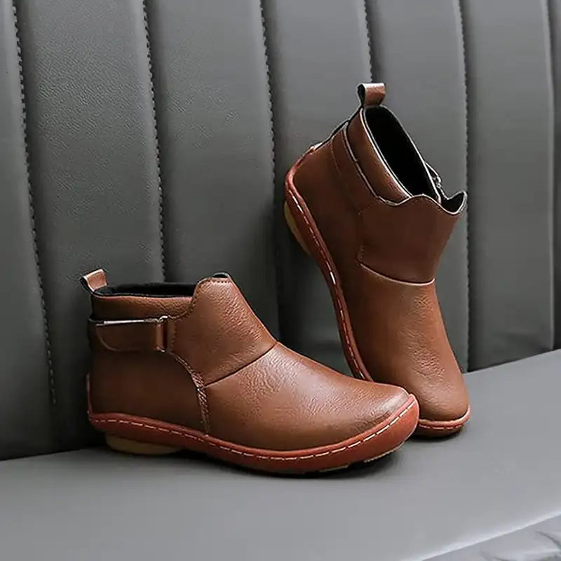 Stivaletti in pelle marrone su divano grigio, design elegante e moderno, ideali per moda autunnale e invernale, calzature uomo e donna.