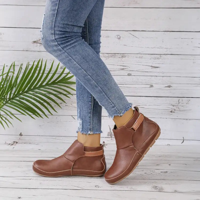 Jeans aderenti e stivaletti in pelle marrone su sfondo di legno bianco, moda casual donna, scarpe autunnali eleganti, stile urbano.