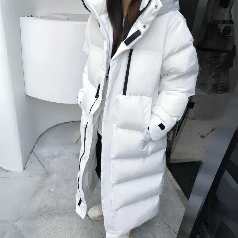 Giacca lunga invernale bianca imbottita, con cappuccio e tasche, indossata da una persona. Stile casual, ideale per il freddo.