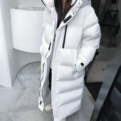 Giacca lunga invernale bianca imbottita, con cappuccio e tasche, indossata da una persona. Stile casual, ideale per il freddo.