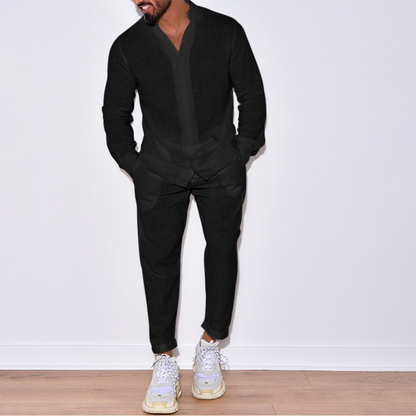 Uomo in abito nero casual, camicia e pantaloni coordinati, scarpe da ginnastica bianche, posa su pavimento in legno, moda maschile elegante.