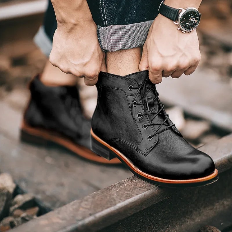 Scarponcini neri in pelle su rotaie, uomo con orologio regola i lacci. Moda maschile, calzature eleganti, stile casual autunnale.
