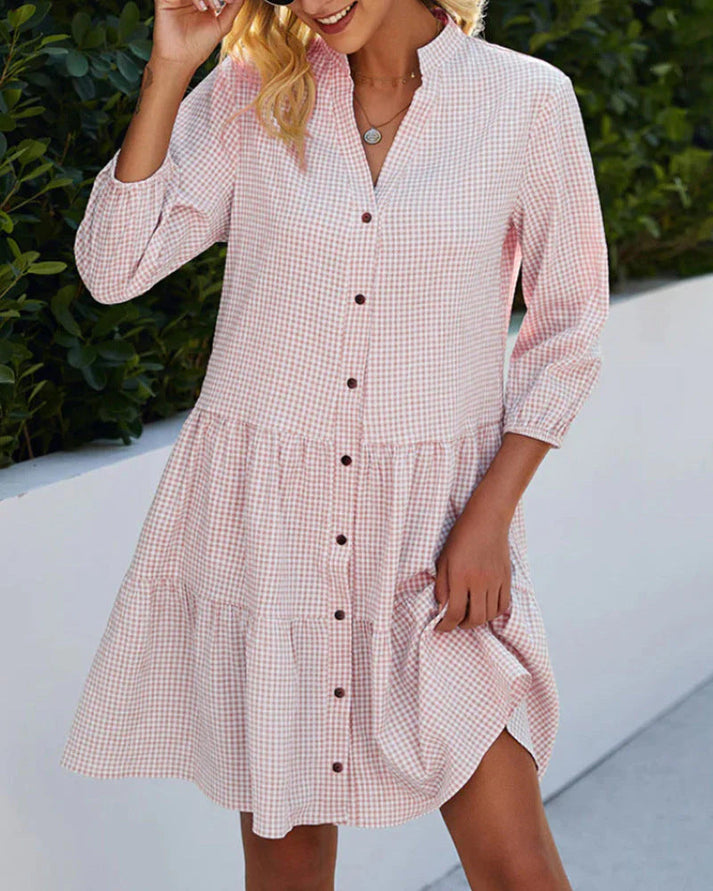 Donna con abito a quadretti rosa e bianco, maniche lunghe, bottoni frontali, in giardino. Moda femminile estiva, stile casual elegante.