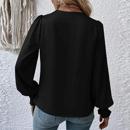 Donna con camicetta nera a maniche lunghe, vista posteriore, indossa jeans. Sfondo con parete bianca e decorazione tessile. Moda casual elegante.