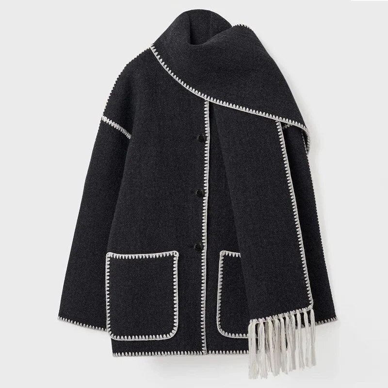 Cappotto nero in lana con dettagli bianchi, tasche frontali e sciarpa integrata con frange. Elegante e caldo, ideale per l'inverno.