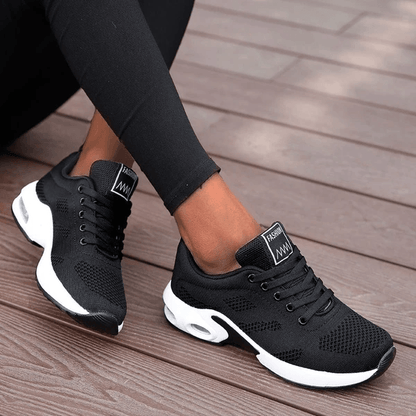 Scarpe da ginnastica nere da donna su pavimento in legno, design moderno e traspirante, ideali per sport e tempo libero.