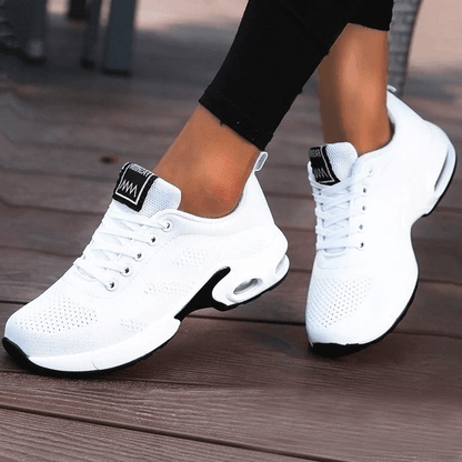 Scarpe da ginnastica bianche da donna su pavimento in legno, design moderno e traspirante, ideali per sport e tempo libero, comfort e stile.